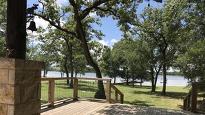 A wooden deck with a stone wall, overlooking a grassy area and a body of water. - Hidden Piece of Heaven on Lake Limestone (Thornton)
