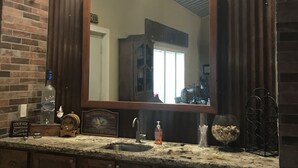 A bathroom with a large mirror, a sign above it reading "The GOATS", a bottle of liquor, a soap dispenser, and a glass bowl on the counter. - Hidden Piece of Heaven on Lake Limestone (Thornton)