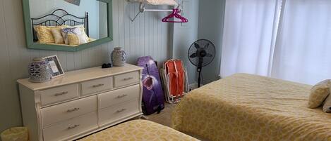 A bedroom with two beds, a dresser, a mirror, a fan, and a window with curtains.