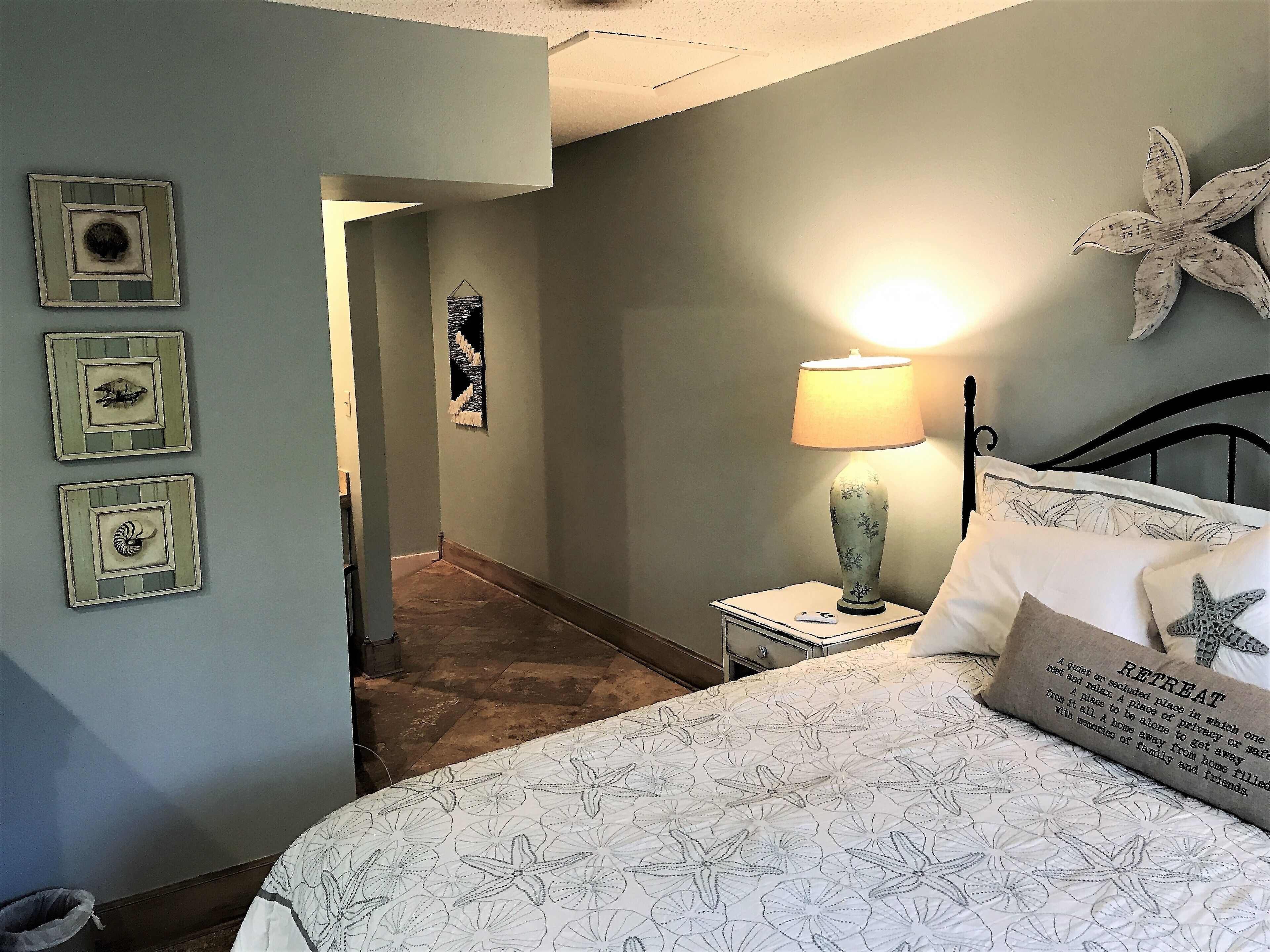 A bedroom with a bed, a nightstand, a lamp, and wall art.