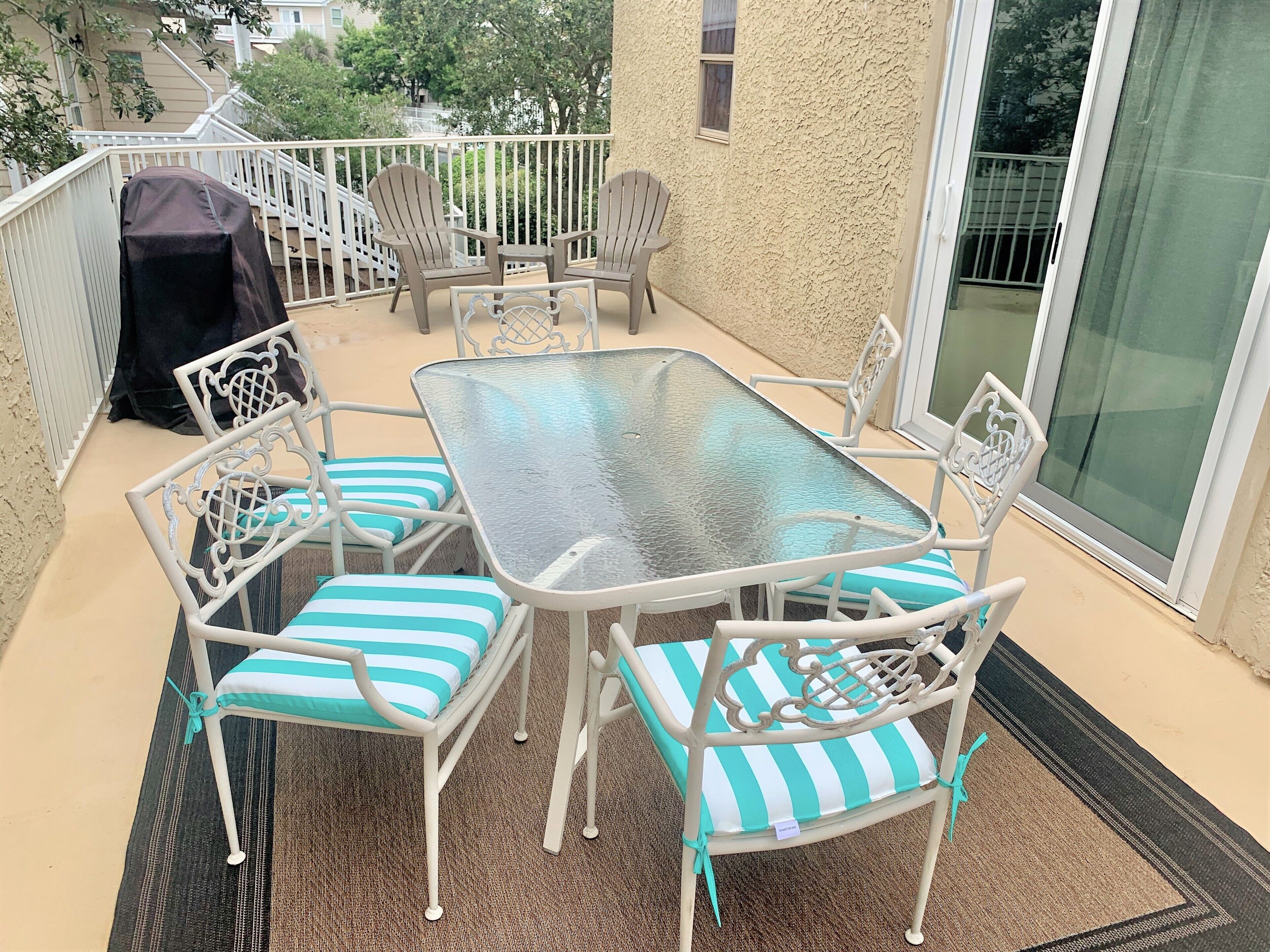 Eine Terrasse mit Glastisch und gestreiften Stühlen, ein überdachter Grill und im Hintergrund ein Blick auf ein Gebäude.
