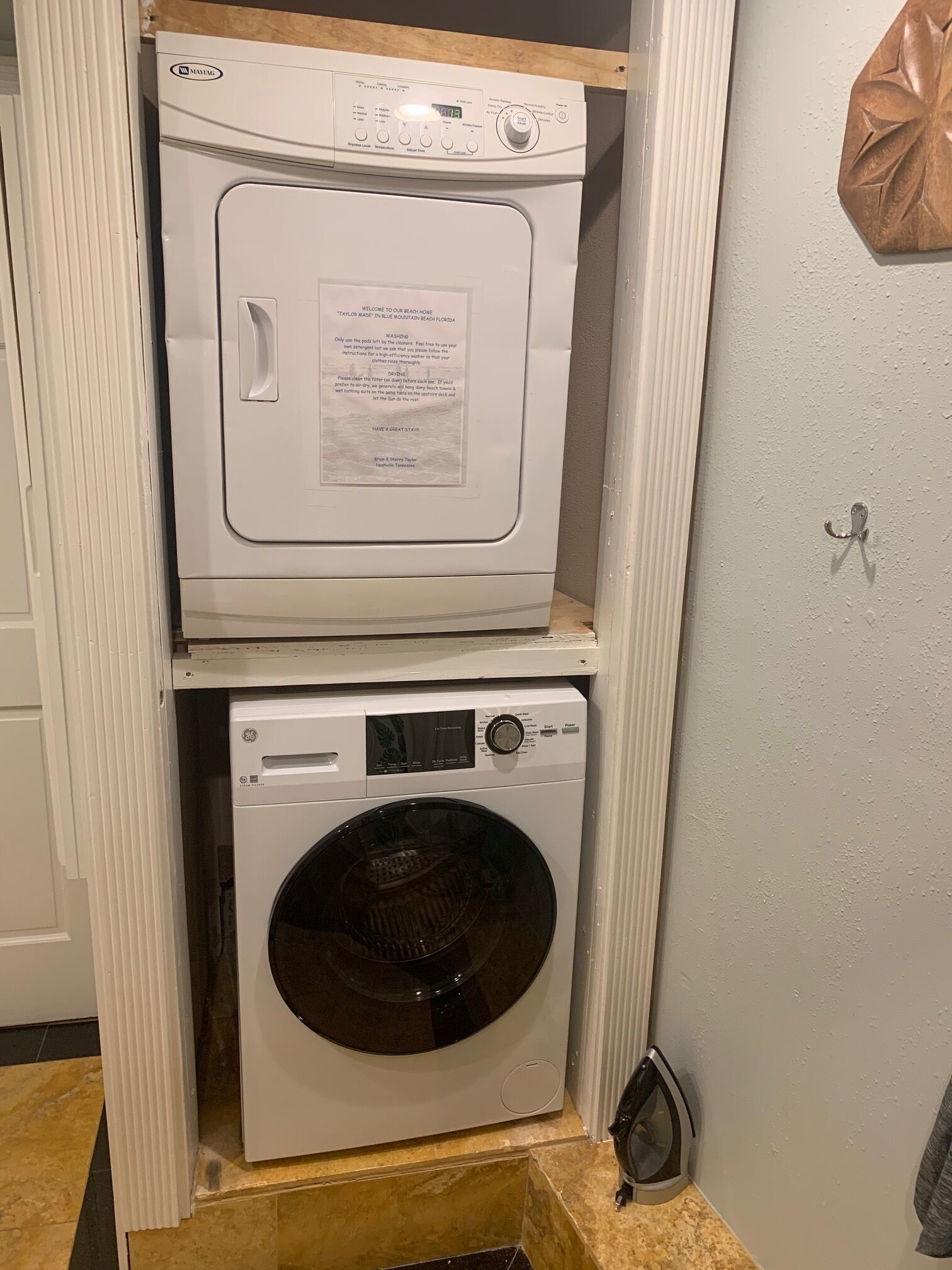 A stacked washer and dryer unit in a laundry room with a wooden countertop and a towel rack on the wall.