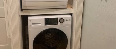 A stacked washer and dryer unit in a laundry room with a wooden countertop and a towel rack on the wall.