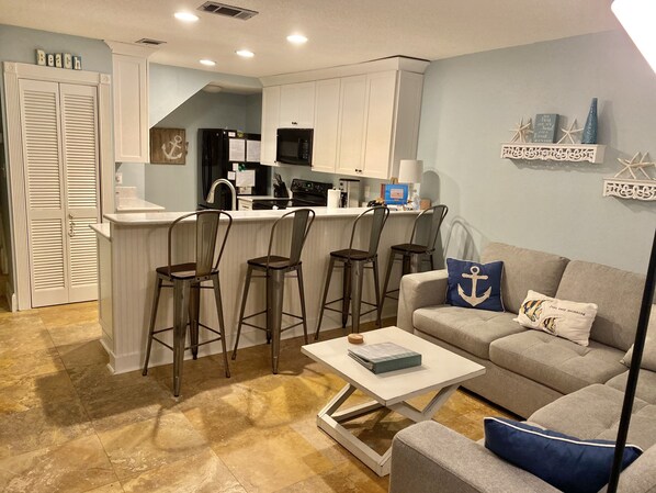 Un espacio habitable compacto con kitchenette, una zona de comedor con taburetes de bar y un rincón de estar con sofá y mesa de centro.