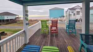 A wooden deck with colorful Adirondack chairs, a view of the beach, and houses in the background. - Just steps to the Sand & Surf!  Sleeps 12, with 2 Master Suites! Perfect Rental! (Bolivar Peninsula)