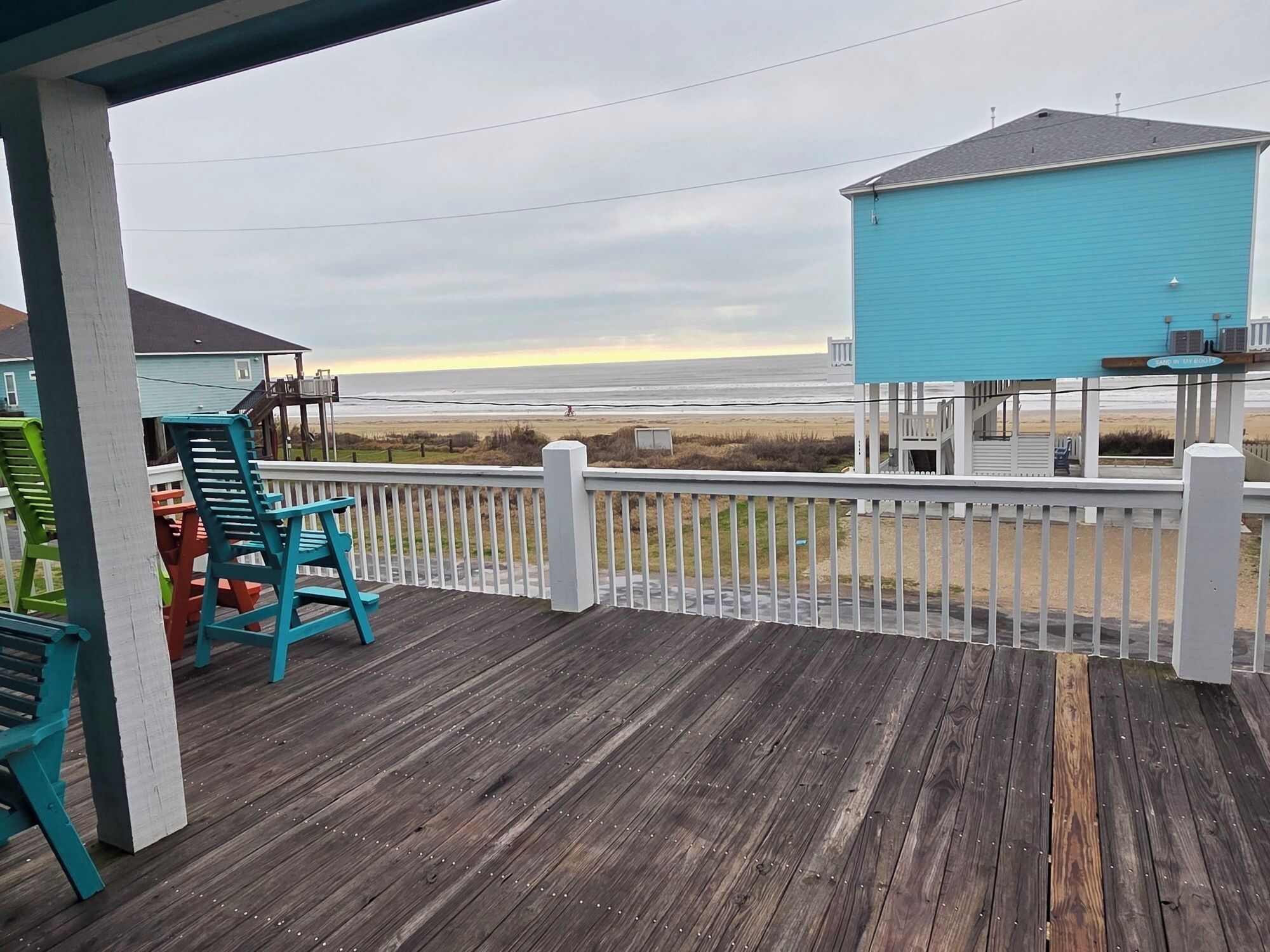A wooden deck with chairs, a view of the beach, and a blue building.