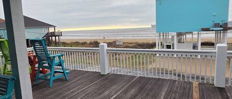A wooden deck with chairs, a view of the beach, and a blue building.