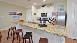 A kitchen with a granite countertop, white cabinets, stainless steel appliances, and a wooden bar stool. - Just steps to the Sand & Surf!  Sleeps 12, with 2 Master Suites! Perfect Rental! (Bolivar Peninsula)