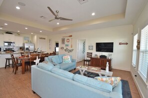 Un salón espacioso con un amplio sofá azul claro, un comedor con mobiliario de madera, una cocina con armarios blancos y un ventilador de techo.