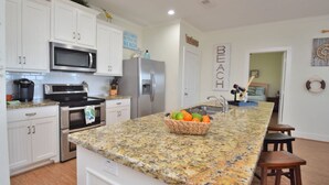A kitchen with white cabinets, stainless steel appliances, a granite countertop, and a fruit bowl. - Just steps to the Sand & Surf!  Sleeps 12, with 2 Master Suites! Perfect Rental! (Bolivar Peninsula)