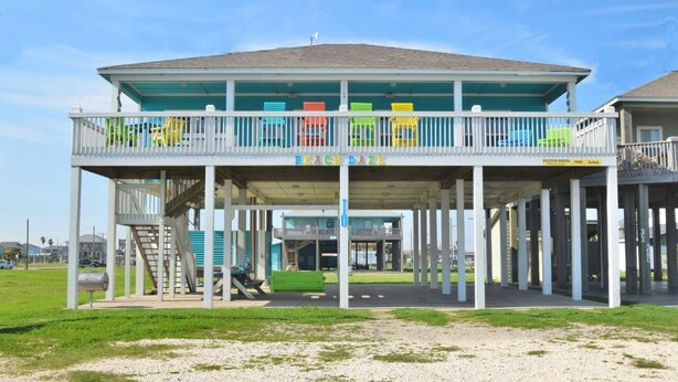 A beachside building with a covered deck and multiple colorful chairs. - Just steps to the Sand & Surf!  Sleeps 12, with 2 Master Suites! Perfect Rental! (Bolivar Peninsula)