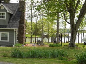 Una casa con chimenea de piedra, un muelle que se adentra en un lago y un área de picnic con mesas y sillas.