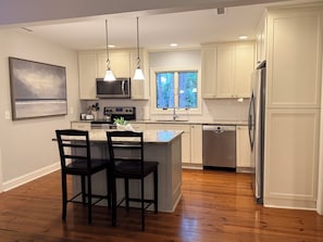 A modern kitchen with a central island, stainless steel appliances, and a window with a view of trees.