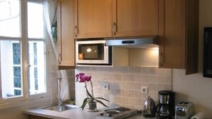 Une cuisine compacte dotée de meubles en bois, d’un four à micro-ondes encastré, d’une machine à laver, d’une machine à café et d’un grille-pain.