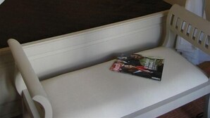 Un lit avec des rideaux blancs, une table de chevet avec une lampe et un magazine posé sur le lit.