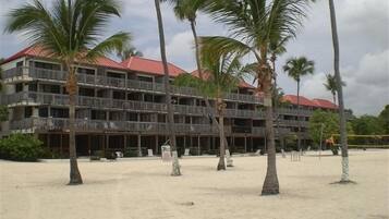 A multi-story hotel with balconies, located on a sandy beach with palm trees.