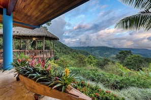 A wooden structure with a thatched roof, surrounded by lush greenery and a view of distant mountains. - Stunning Ocean View-Rainforest Villa. Concierge, Breakfast/Housekeeping M-F. (Uvita, Costa Rica)