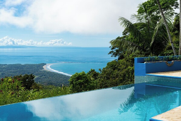 A clear view of a swimming pool with a view of the ocean and a beach.