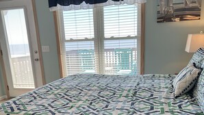 A bedroom with a large bed, a window with blinds, a door, and a painting on the wall.