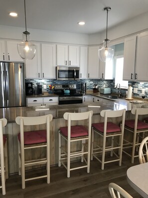 Cozinha moderna com armários brancos, eletrodomésticos de aço inoxidável e uma ilha central com banquetas.