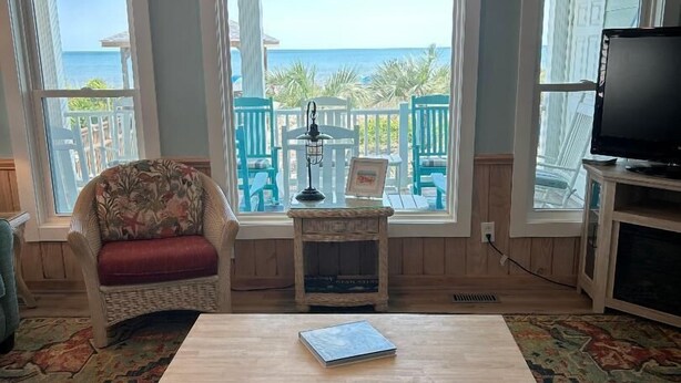 A living room with a view of the ocean, a wicker chair, a wooden coffee table, and a television.
