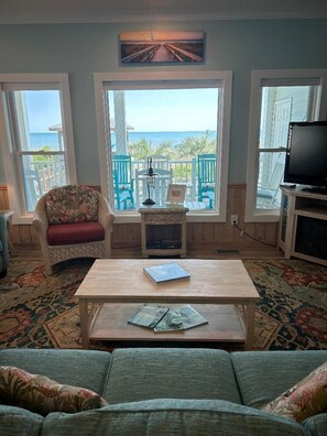 Ein Wohnzimmer mit Meerblick, ein Korbstuhl, ein Holztisch und ein Fernseher.