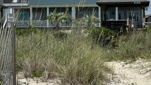 A large beachfront house with a covered porch and a fenced deck area.