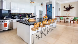 Cozinha moderna com ilha central, banquetas e área de jantar com cadeiras.