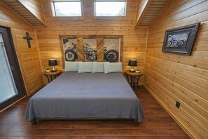 A wooden room with a bed, two nightstands, a cross on the wall, and a motorcycle painting. - Beautiful Log cabin overlooking a meadow (Pipe Creek)