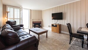 A living room with a leather sofa, a coffee table, a fireplace, a TV mounted on the wall, and a dining area with a table and chairs. - Paradise found in Oceanside with panoramic ocean view (Oceanside)