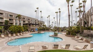 A resort pool area with lounge chairs and palm trees. - Paradise found in Oceanside with panoramic ocean view (Oceanside)