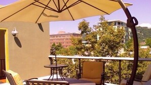 Un balcon doté d’un espace extérieur aménagé avec des chaises et une table, le tout abrité par un grand parasol.