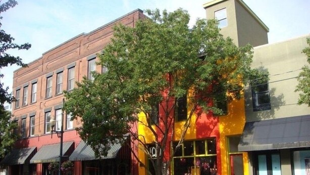 Une vue de rue avec un bâtiment en briques rouges, une devanture de magasin jaune et rouge, et un arbre à l’avant.