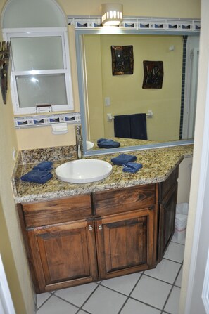 Une salle de bain avec un comptoir en granit, un lavabo blanc, des armoires en bois et un miroir.