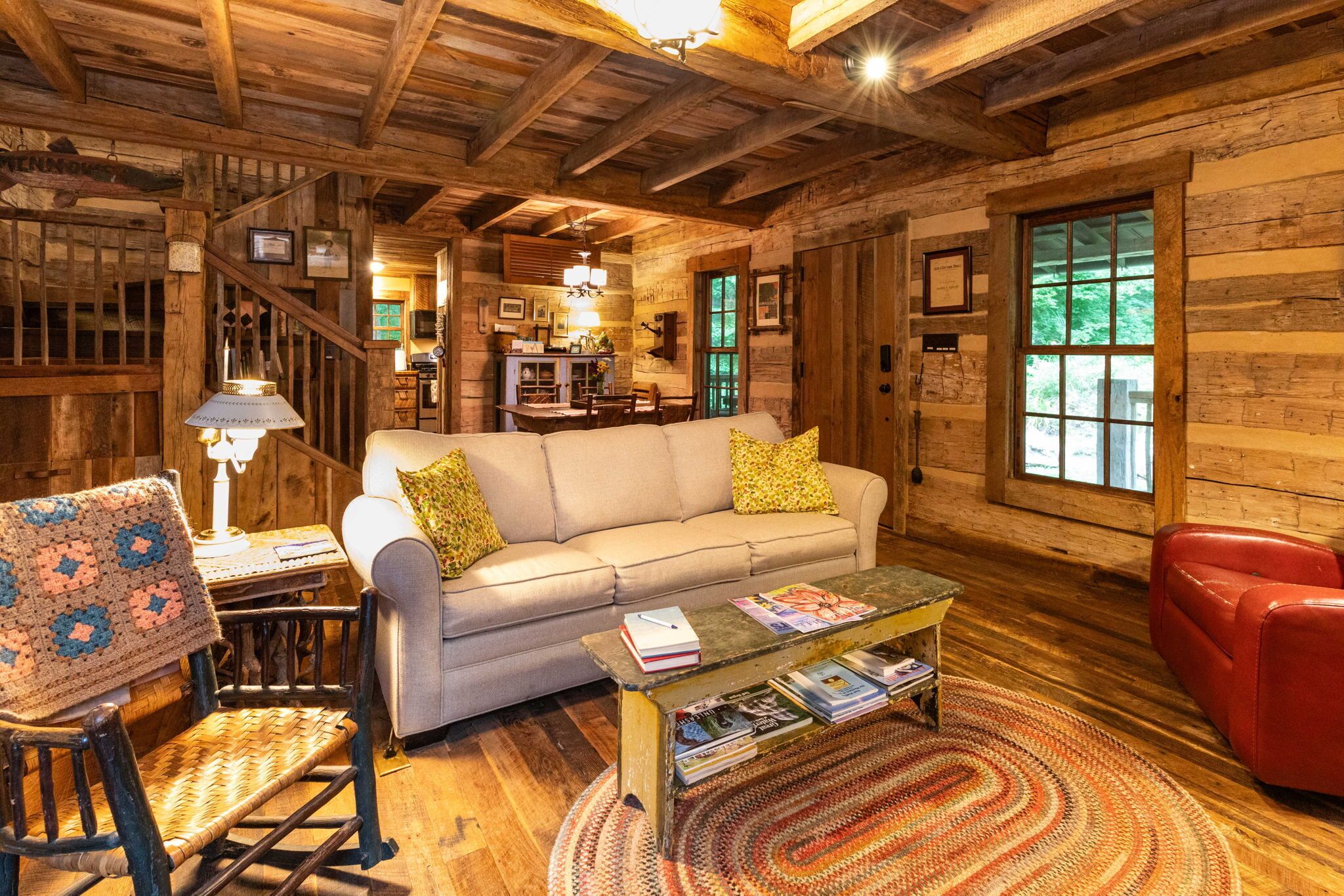 L’intérieur d’un chalet accueillant, avec un canapé, une table basse sur laquelle sont posés des livres, un fauteuil à bascule et un fauteuil rouge.