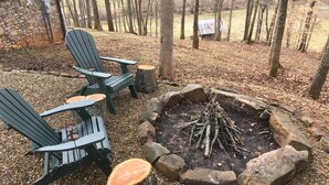 Ein rustikaler Sitzbereich im Freien mit Adirondack-Stühlen und einem Feuerkorb aus Stein, umgeben von einer Steingrenze.