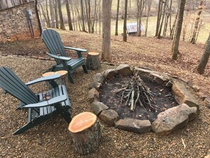 Un'area salotto esterna rustica con poltrone Adirondack e un braciere in pietra circondato da un cordolo di rocce.