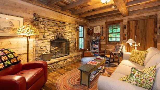 Ein gemütliches Wohnzimmer mit Kamin aus Stein, Ledermöbeln und Holzbalken.