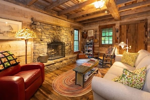 A cozy living room with a stone fireplace, leather furniture, and wooden beams. - Eli Reeves Cabin at Hobbyknob Farm - Authentically restored 1820 Log Cabin (Weaverville)