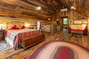 Una stanza rustica in legno con un letto, una panca, un divano rosso e un tappeto decorato.