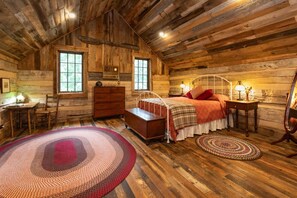A rustic log cabin bedroom with a wooden bed, dresser, and two windows.