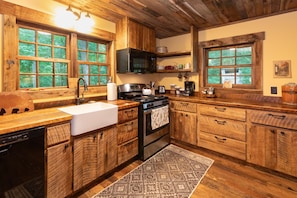 Una cucina con mobili in legno, un fornello, un lavandino e due finestre con vista sugli alberi.