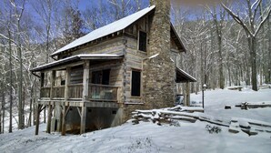 Eine Blockhütte mit Stein Fundament, einer Holzterrasse und einem mit Schnee bedeckten Dach.
