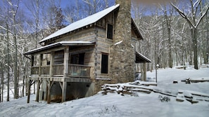 Una baita di legno con fondamenta in pietra, un portico in legno e un tetto imbiancato dalla neve.