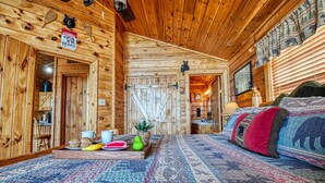 A cozy cabin interior with wooden walls, a bed with patterned bedding, a breakfast tray, and a bear-themed sign.