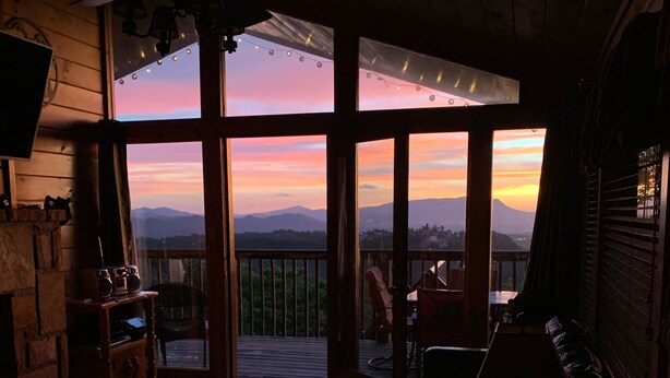 A cozy cabin interior with a large sliding glass door leading to a balcony, offering a view of distant mountains.