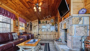 A cozy cabin interior with a wooden ceiling, stone fireplace, leather sofa, and a dining area.