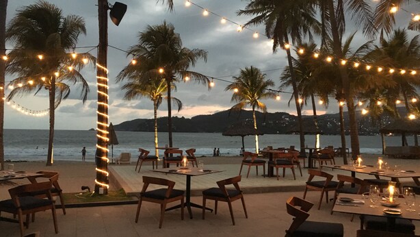 An outdoor dining area with tables and chairs, string lights, and palm trees. - <br>Private beach Exclusive Beach Zihuatanejo, direct access La Ropa RVILLAS SOL (ZIHUATANEJO)