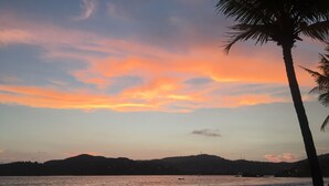 A beach with a sunset, palm trees, and distant hills. - <br>Private beach Exclusive Beach Zihuatanejo, direct access La Ropa RVILLAS SOL (ZIHUATANEJO)