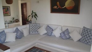 A white sectional sofa with patterned cushions, a blue-tiled coffee table, and a painting of a snail on the wall. - <br>Private beach Exclusive Beach Zihuatanejo, direct access La Ropa RVILLAS SOL (ZIHUATANEJO)